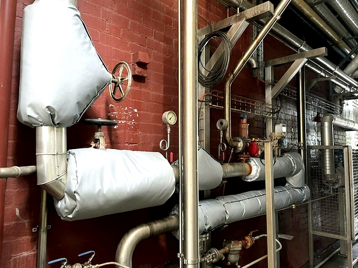Thermal jackets on plant room pipework and valves against a brick wall in an industrial plant room